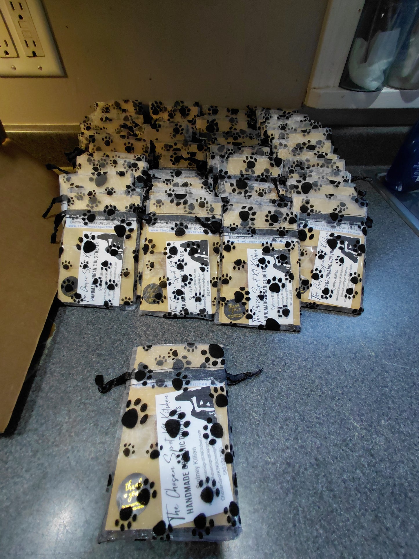 Pile of Bulk Organic Dog Treat Sampler Bags with paw print design on a gray counter