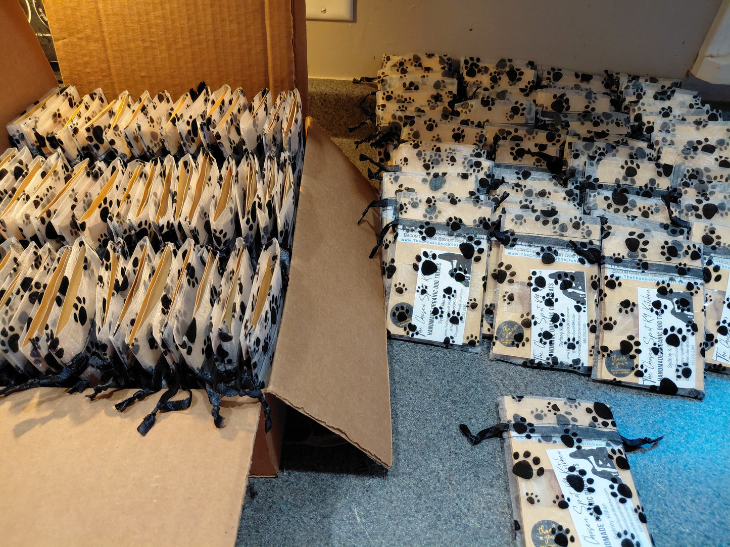 Numerous Bulk Organic Dog Treat Sampler Bags with paw print pattern on mesh baggie placed on a counter and in a carboard box
