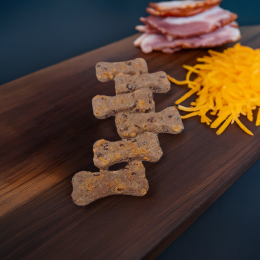 Row of Bacon Cheddar Biscuit Healthy Dog Treats near a pile of shredded cheddar cheese and a stack of bacon