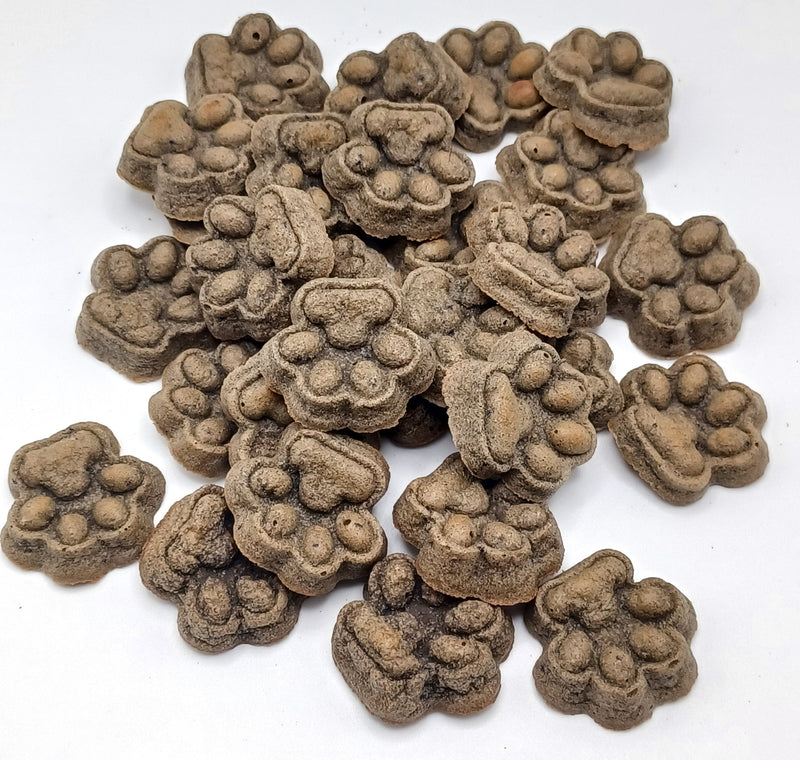 Pile of Liver + Blueberry Dog Treats shaped like paw prints on a white background