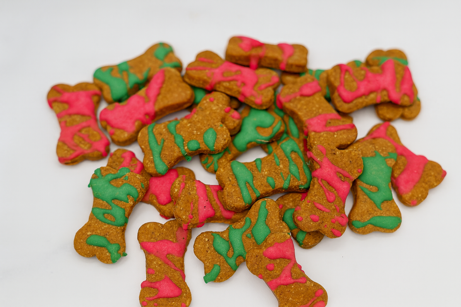 Santa's Dipped Peanut Butter Bones. Handmade organic holiday dog treats from The Chosen Spot K9 Kitchen. Dog bones with green and red icing on a white background.